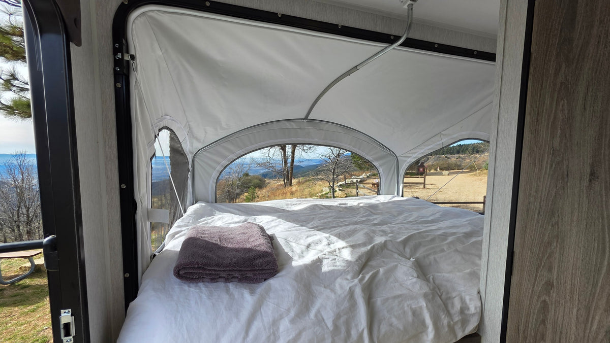 Cozy RV rental pop-up camper bed with a mountain view. White sheets, gray towel on bed. Perfect for scenic getaways. — photo 2