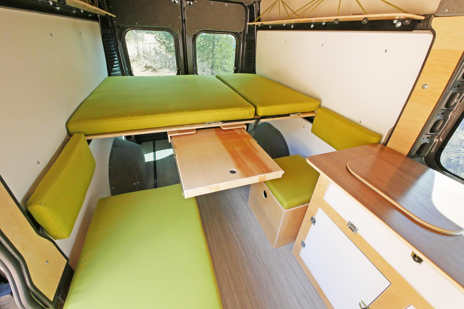 Inside an RV rental: a flexible camper van interior with bright green cushions, two elevated beds, and a pull-out wooden table.