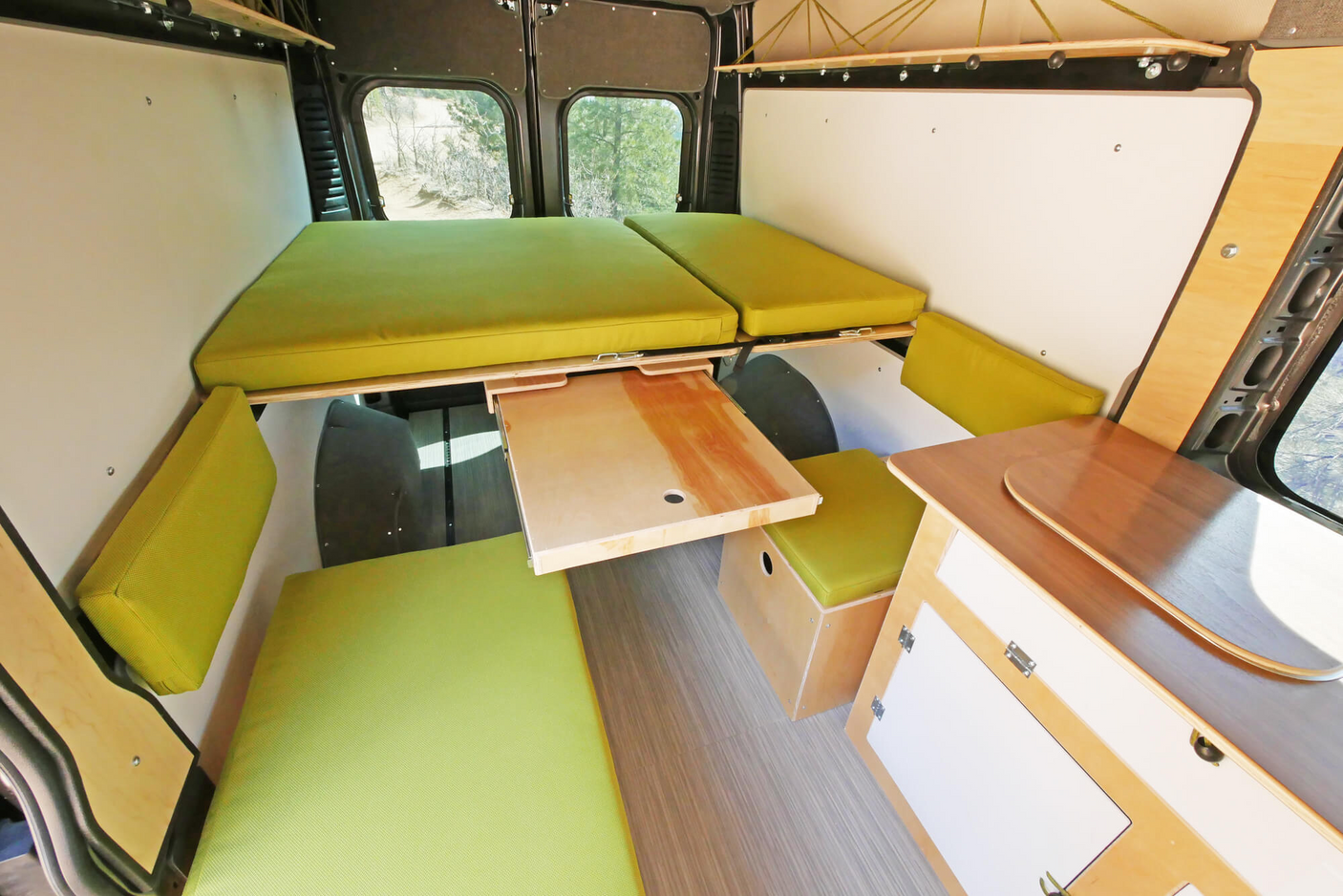 Inside an RV rental: a flexible camper van interior with bright green cushions, two elevated beds, and a pull-out wooden table.