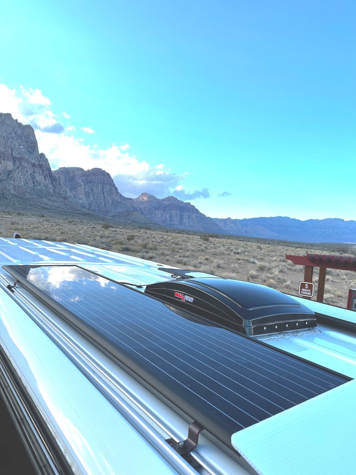 Rooftop solar panels and a MaxxAir fan on an RV rental, set against a scenic desert and mountain backdrop.