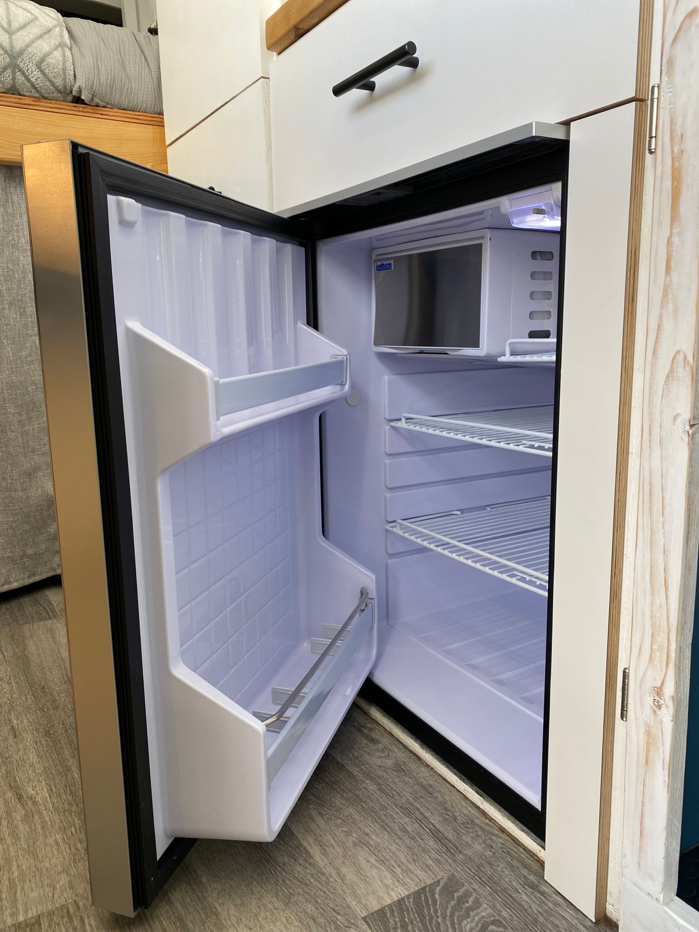This RV rental features an open, clean compact refrigerator with interior shelves, perfect for your journey.