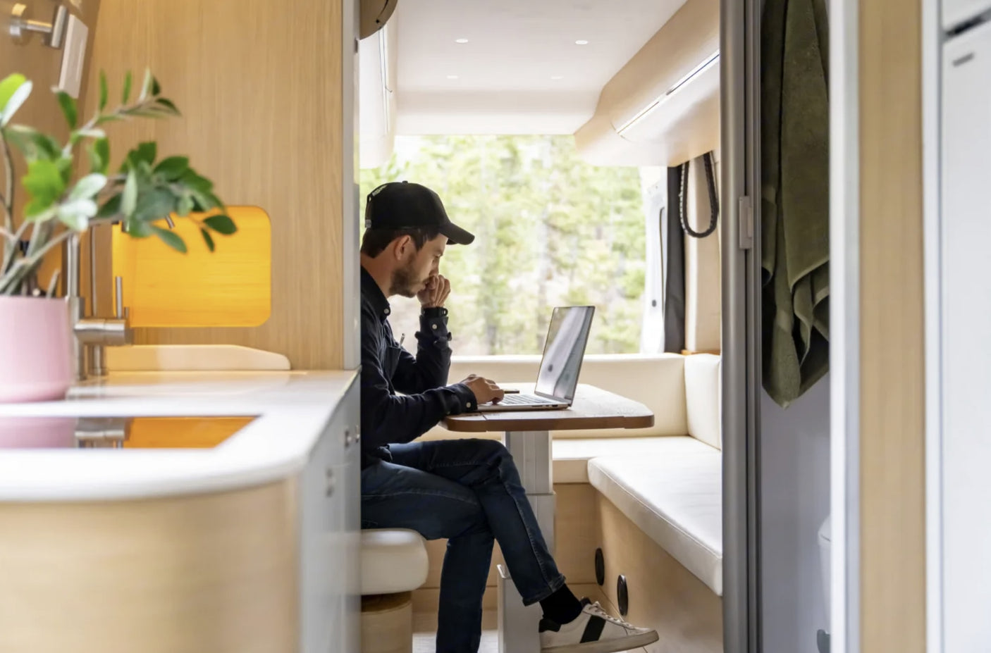 Man works on laptop in a stylish RV rental, featuring light wood interior and nature views. Ideal for remote work.
