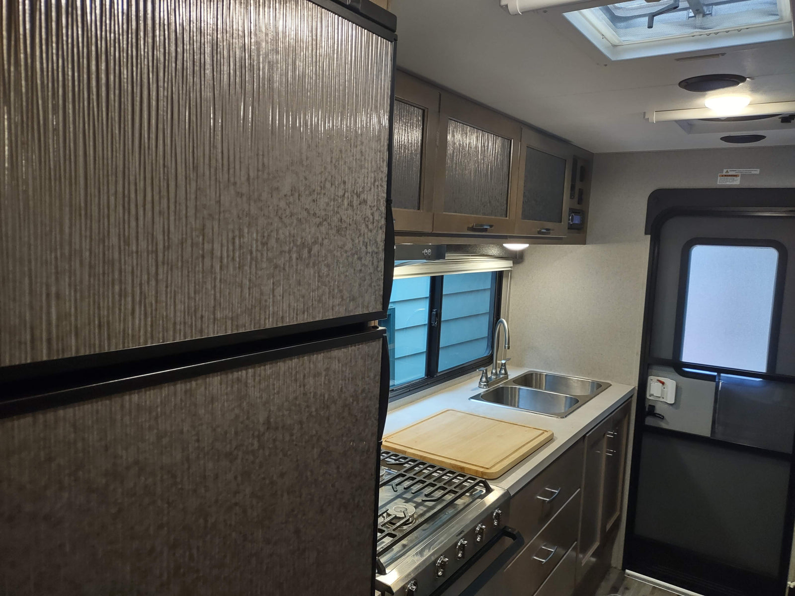 Compact RV rental kitchen interior: stainless steel appliances, dual sink, patterned fridge & cabinets. Ready for travel.