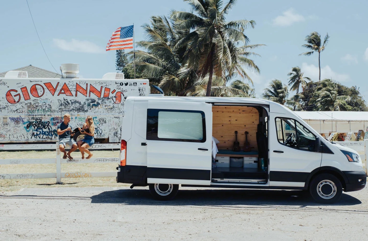 Explore Hawaii van life! An RV rental and people by Giovanni's shrimp truck with palm trees & US flag.