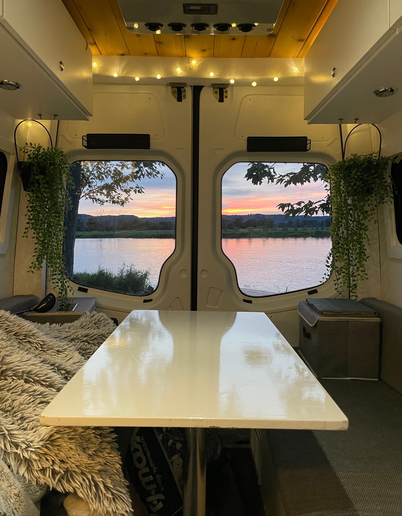Inside a spacious RV rental, watching a vibrant sunset over a river from the comfortable, lamp-lit dining area.