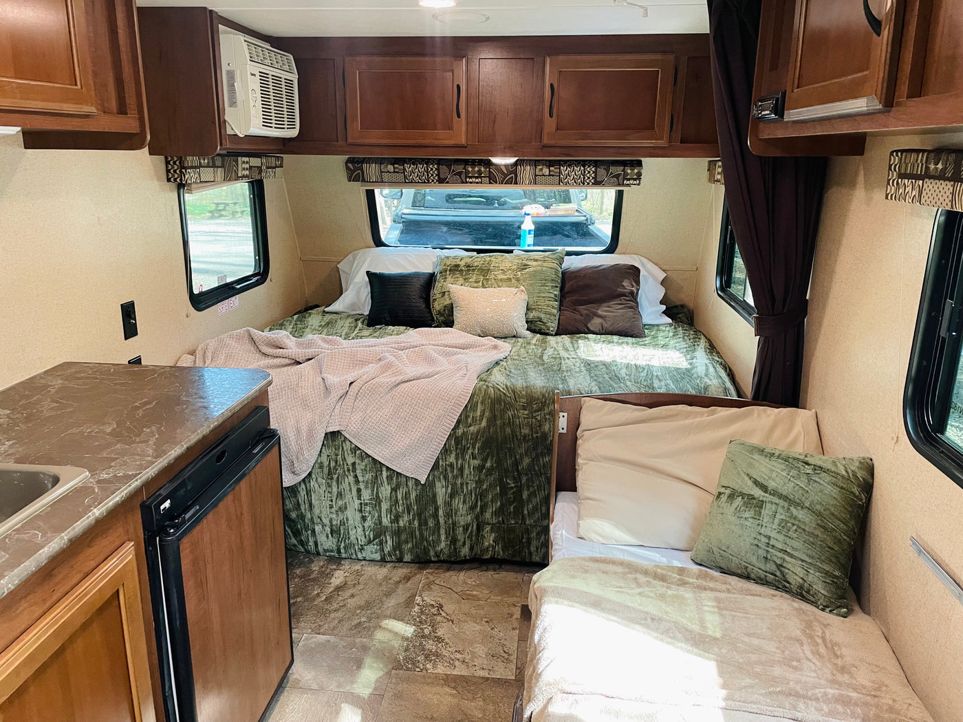 Inside a compact RV rental: a main bed, kitchenette with sink/fridge, AC unit, and a small side bed/couch. — photo 7