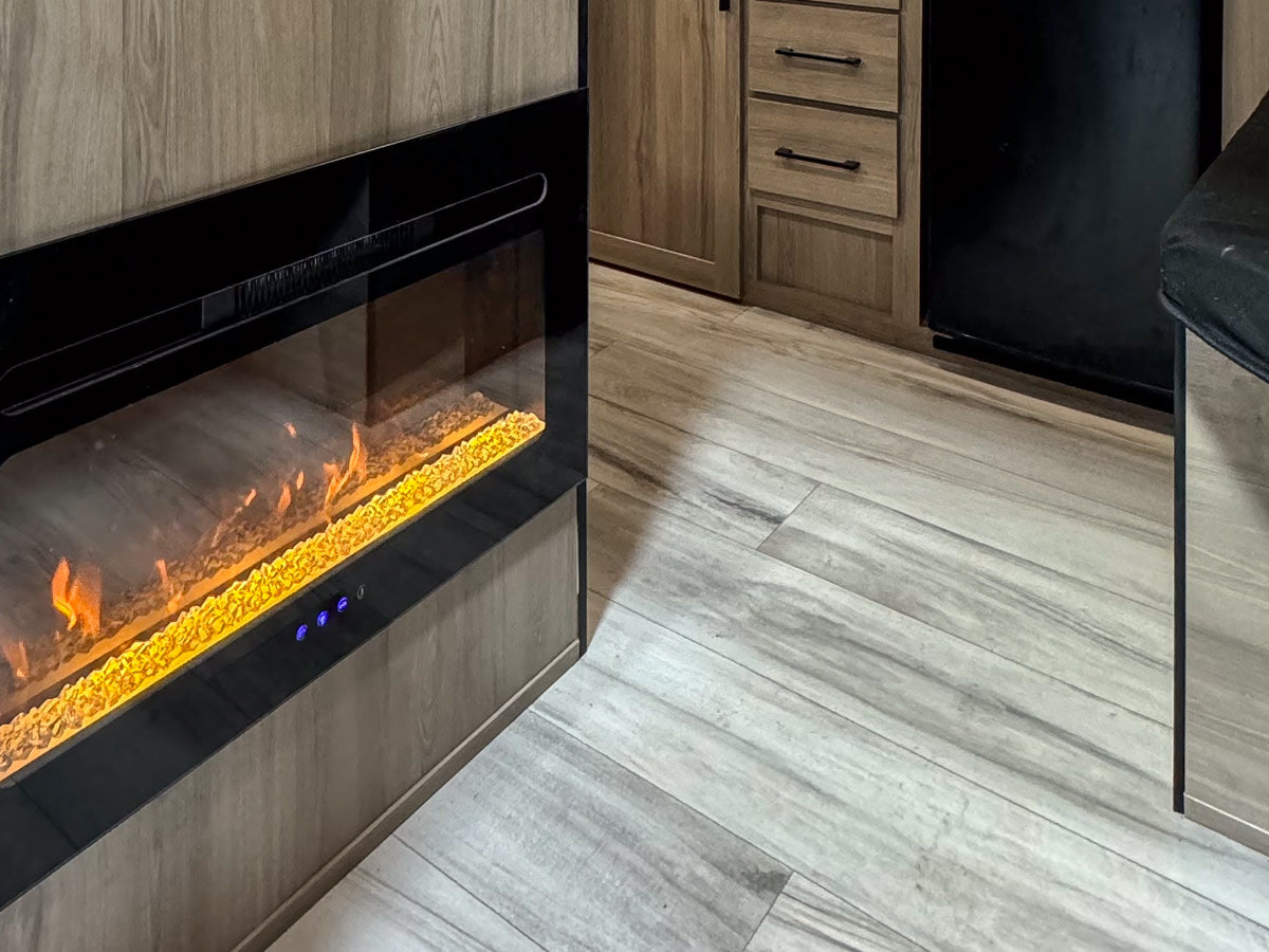 Modern **RV rental** living space: electric fireplace, wood-grain cabinets, and light flooring for comfortable travel.