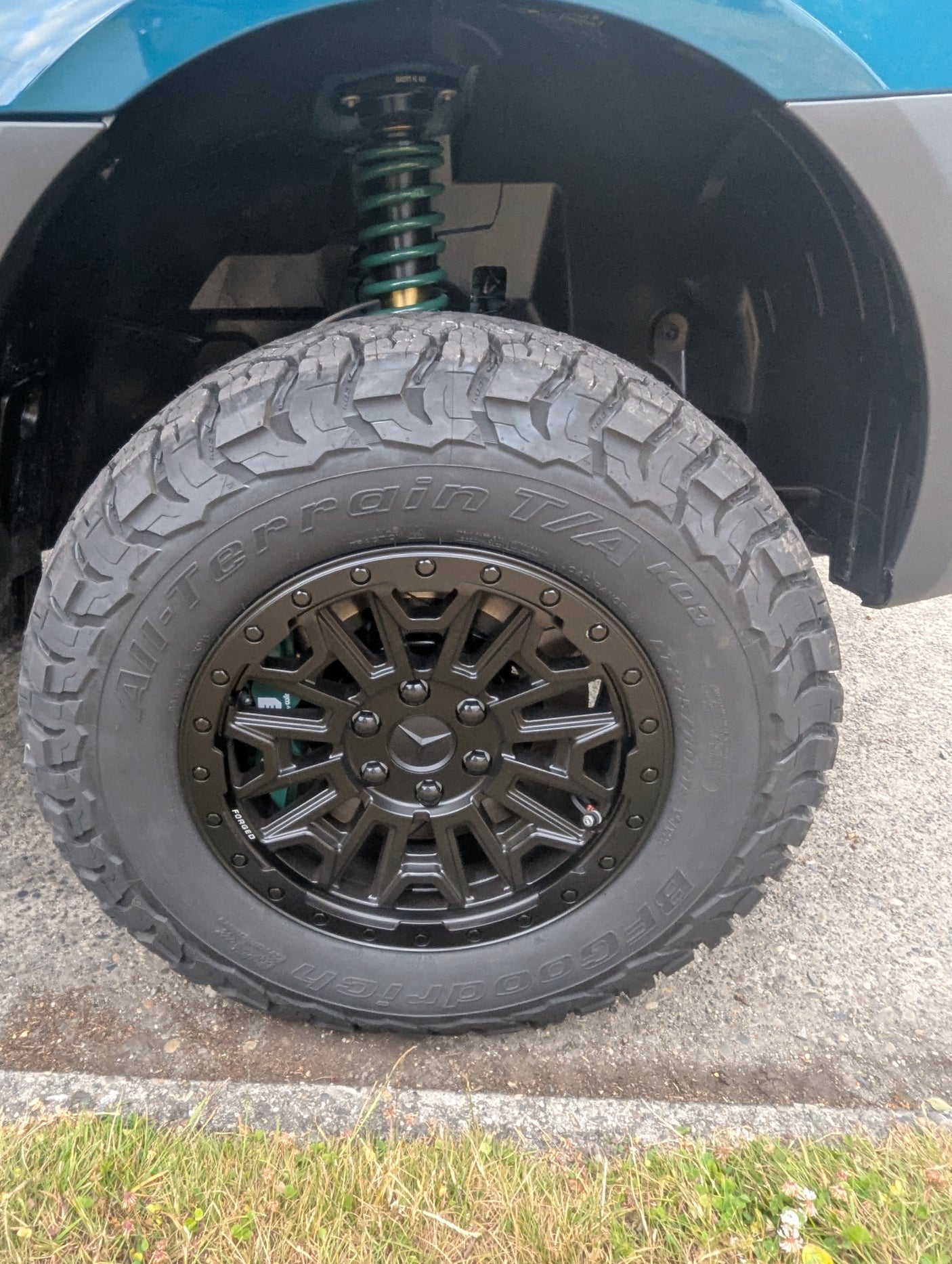 Close-up of a BFGoodrich All-Terrain tire and black forged wheel on an RV rental, showcasing an upgraded green coil suspension.