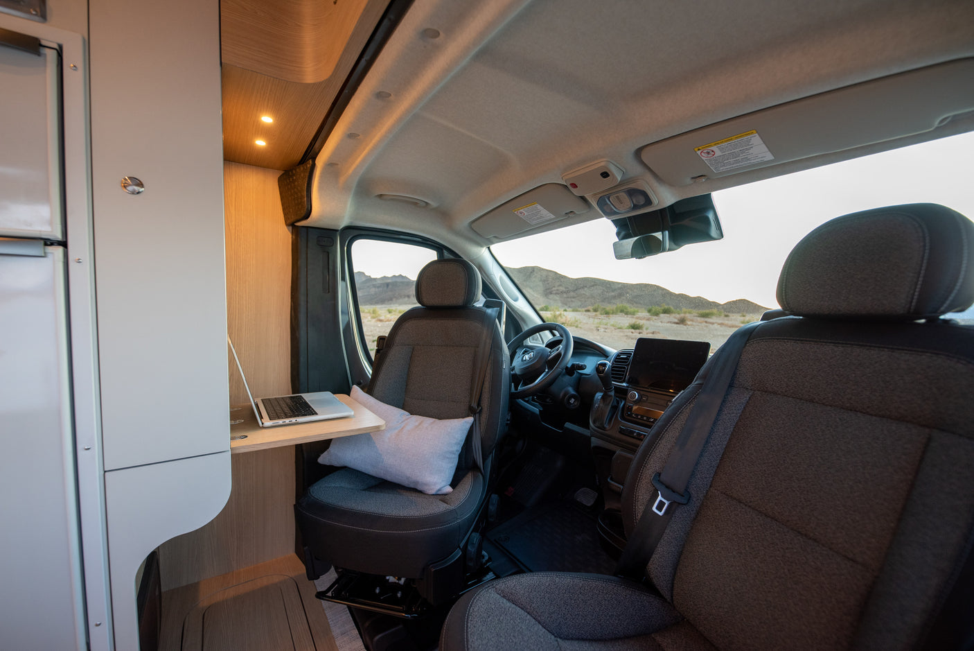 Inside an RV rental: laptop on a pull-out desk by a swivel passenger seat in a camper van, showing a mobile office setup.
