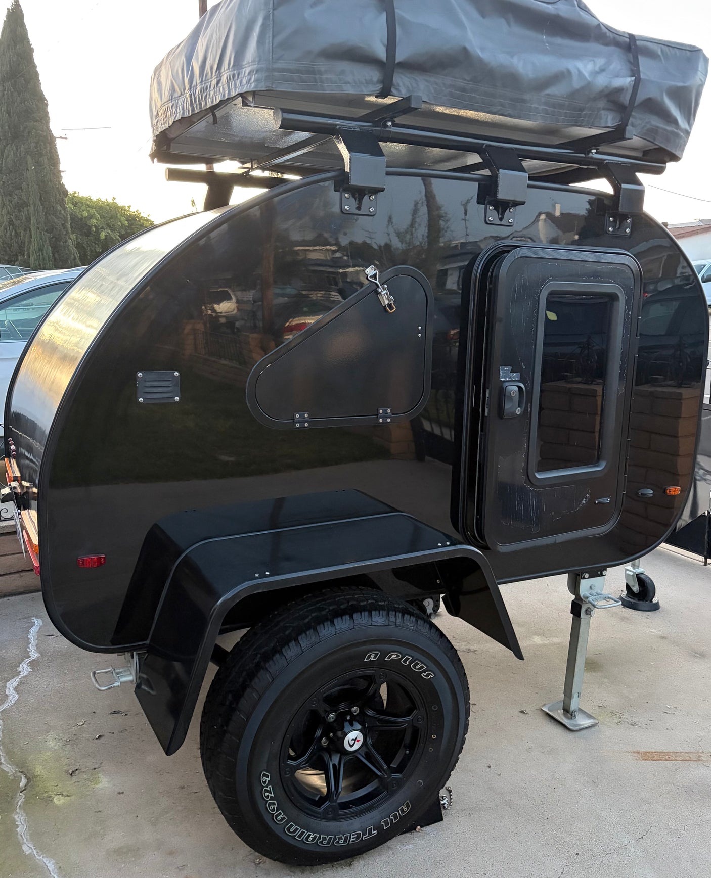 Black teardrop RV rental with rooftop tent, side hatch, and rugged all-terrain tires, ready for adventure.