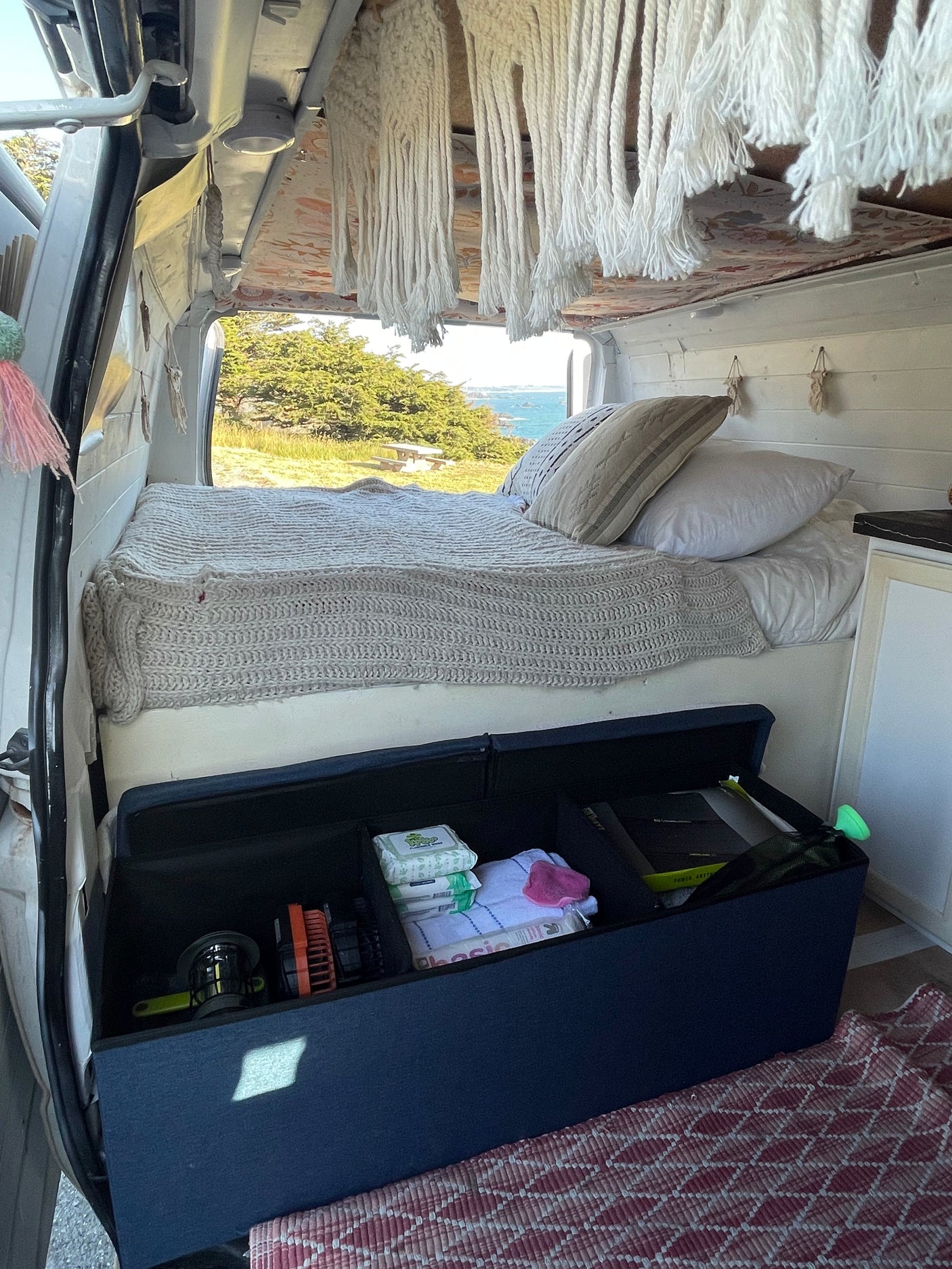 This RV rental offers a cozy bed with a knitted blanket and ocean view. Under-bed storage keeps essentials tidy for travel.