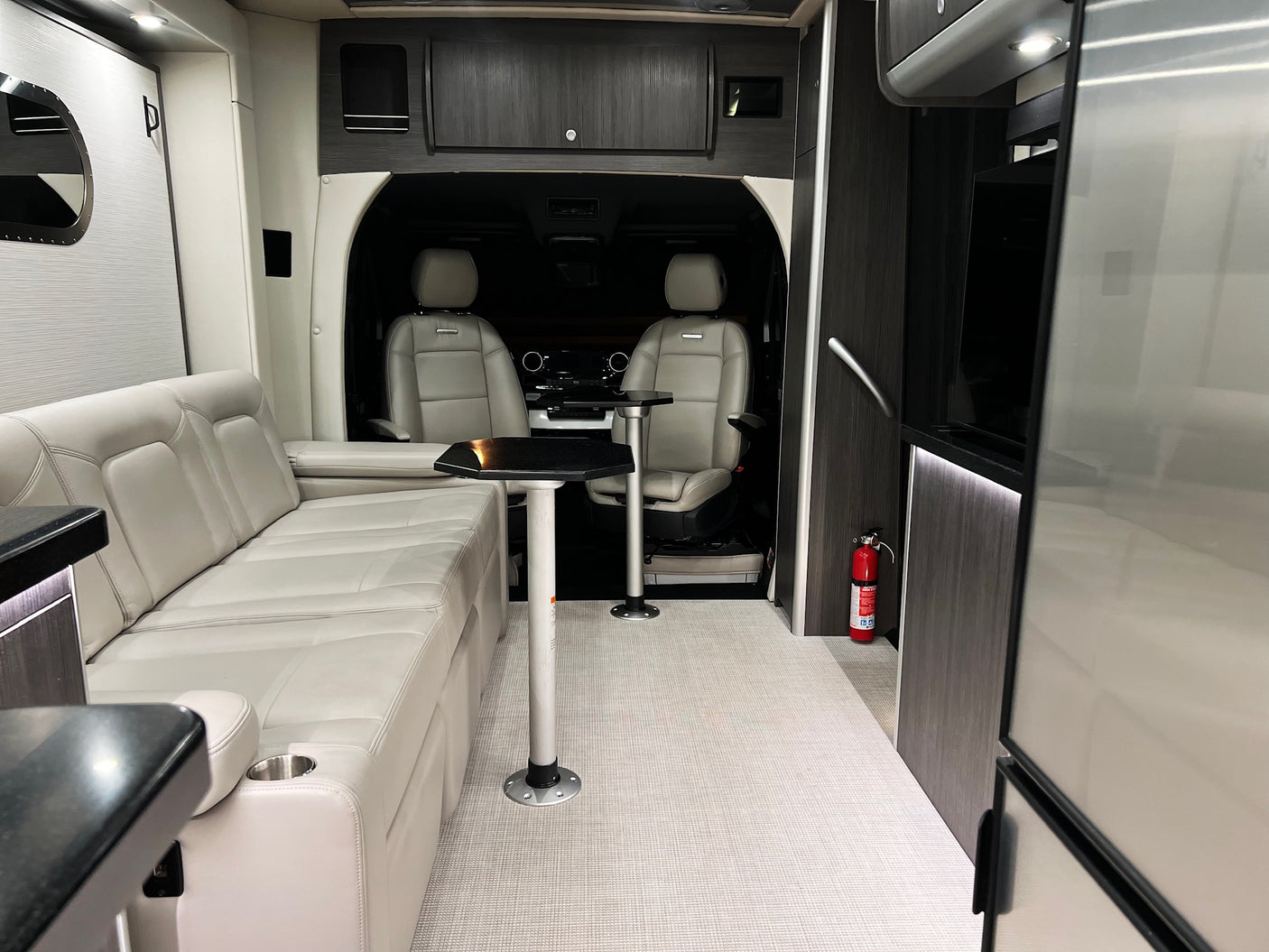 Luxury rv rental interior with plush seating, adjustable tables, front cabin view, and a fire extinguisher for safety.
