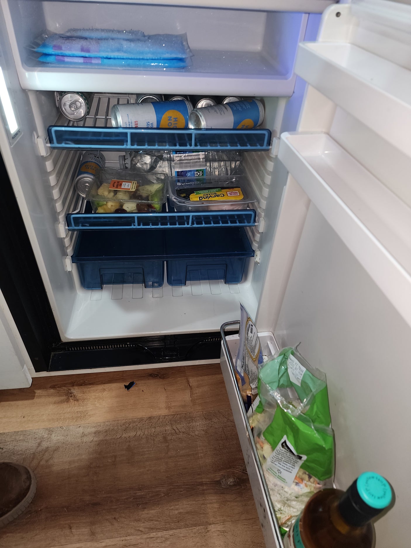Stocked RV rental mini-fridge with seltzers, fruit, and turkey. Ice packs on top, salad on side cart.