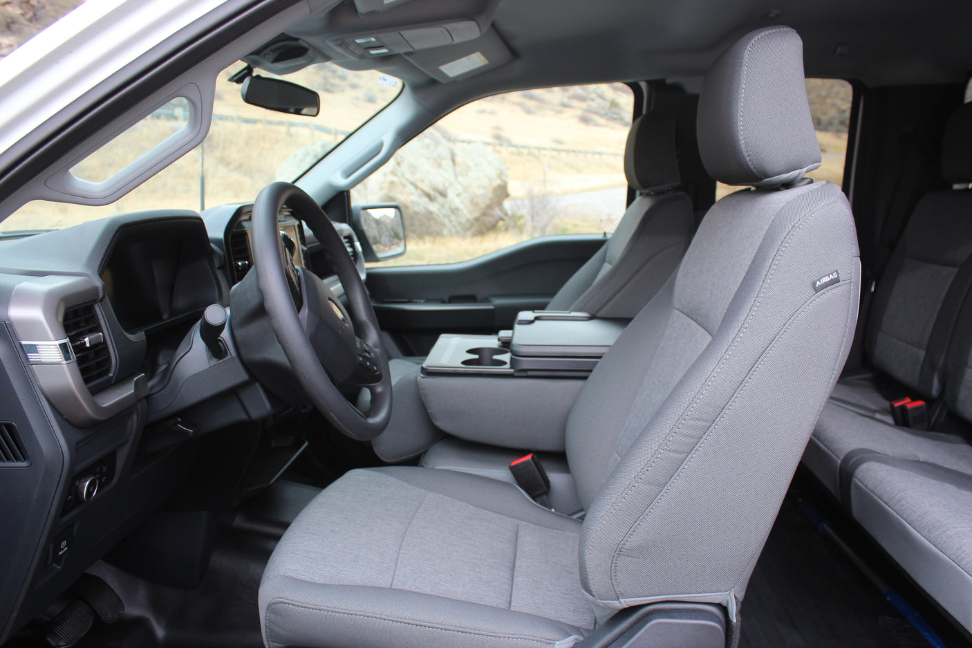 Inside a gray pickup truck, showing fabric seats, steering wheel, and console with cupholders, suitable for an RV rental adventure.