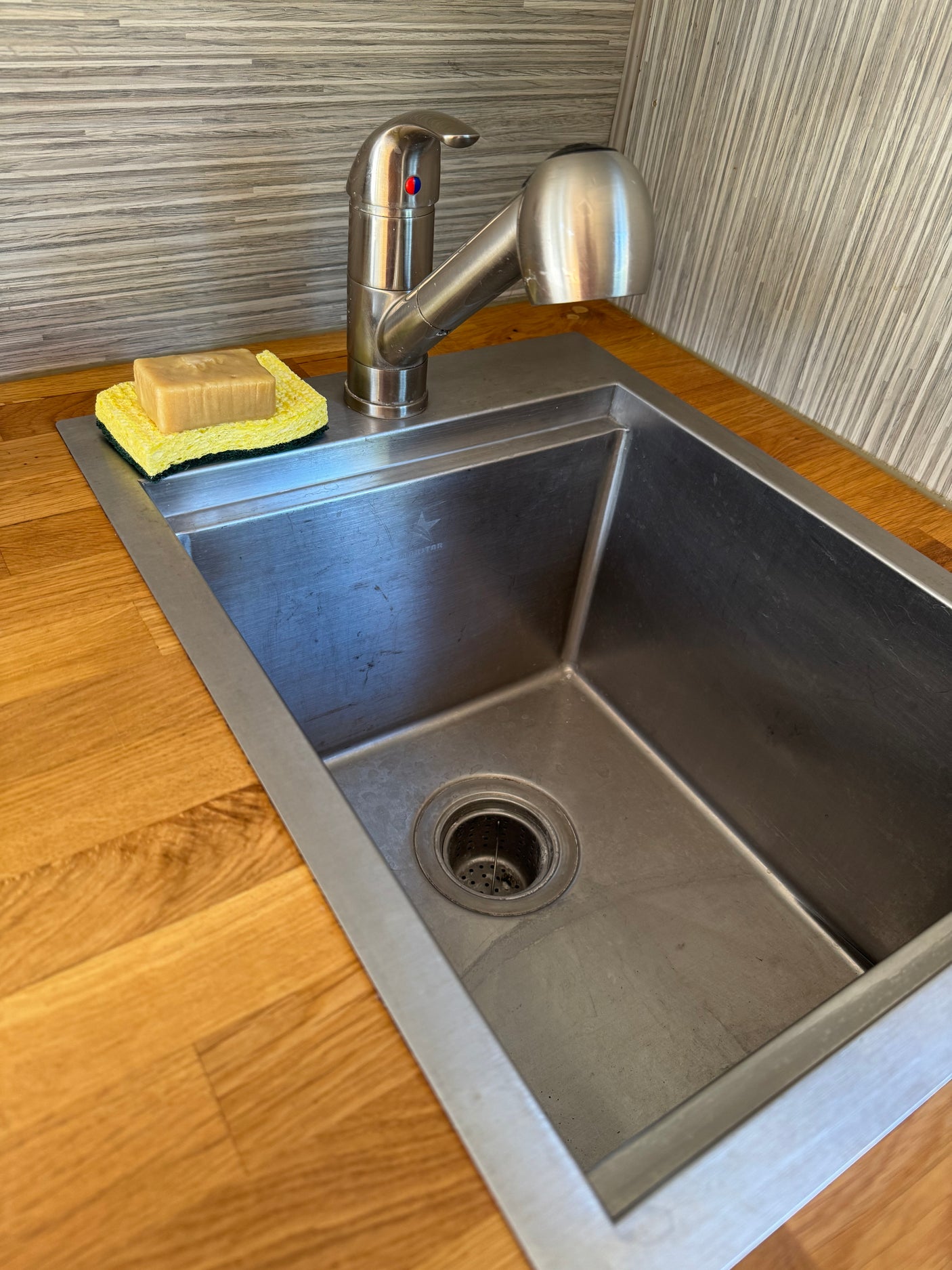 Compact stainless steel sink and pull-down faucet in an RV rental kitchen, with soap and sponge on a wooden counter.