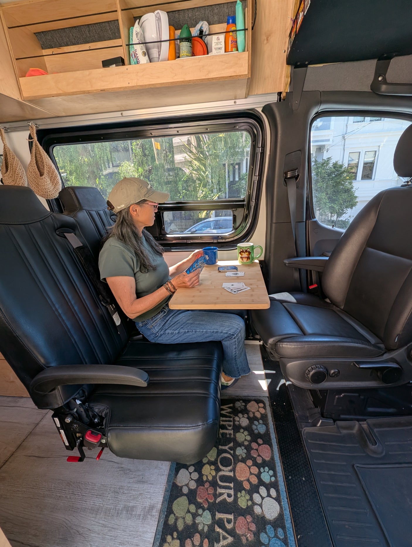Woman playing cards at a table inside an RV rental. Features custom wooden shelves & comfortable seating for travel.