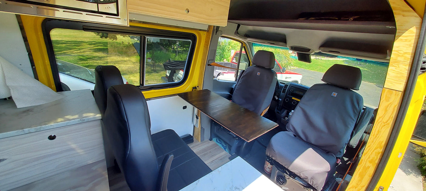 Up-close interior of a yellow custom-built van, showing Carhartt-covered seats and a wooden counter, perfect for an RV rental.