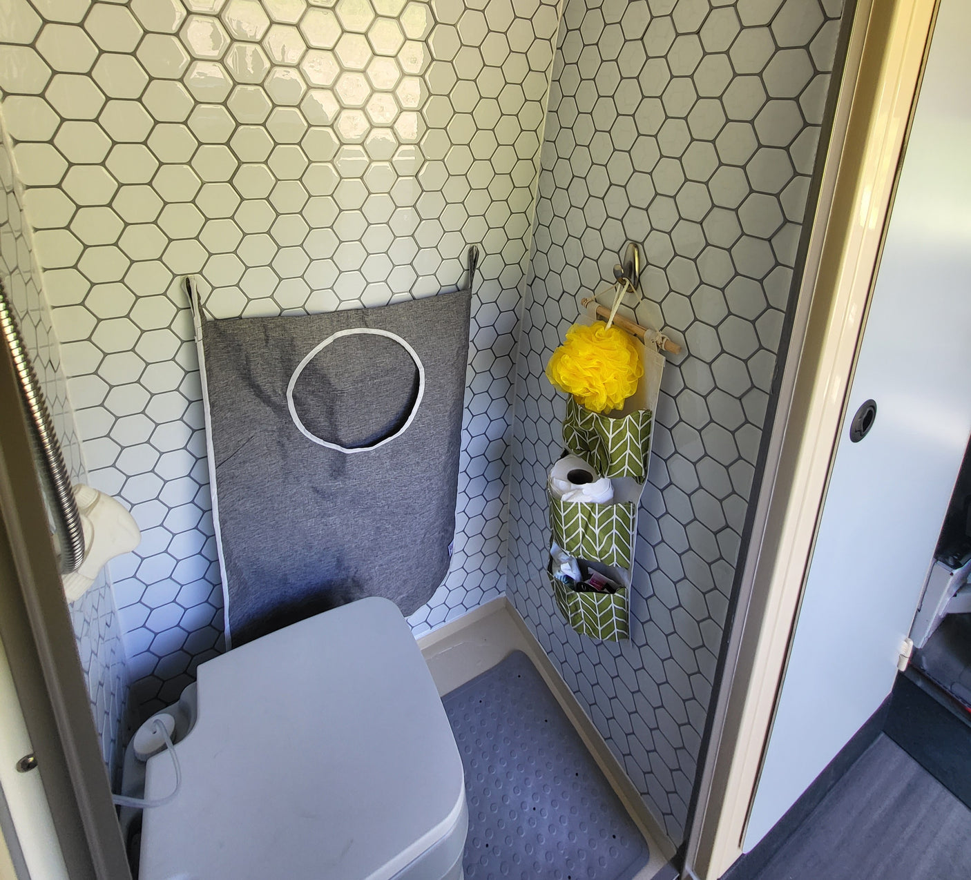 Compact RV rental wet bath with hexagon tiles, portable toilet, handheld shower, and hanging storage solutions.
