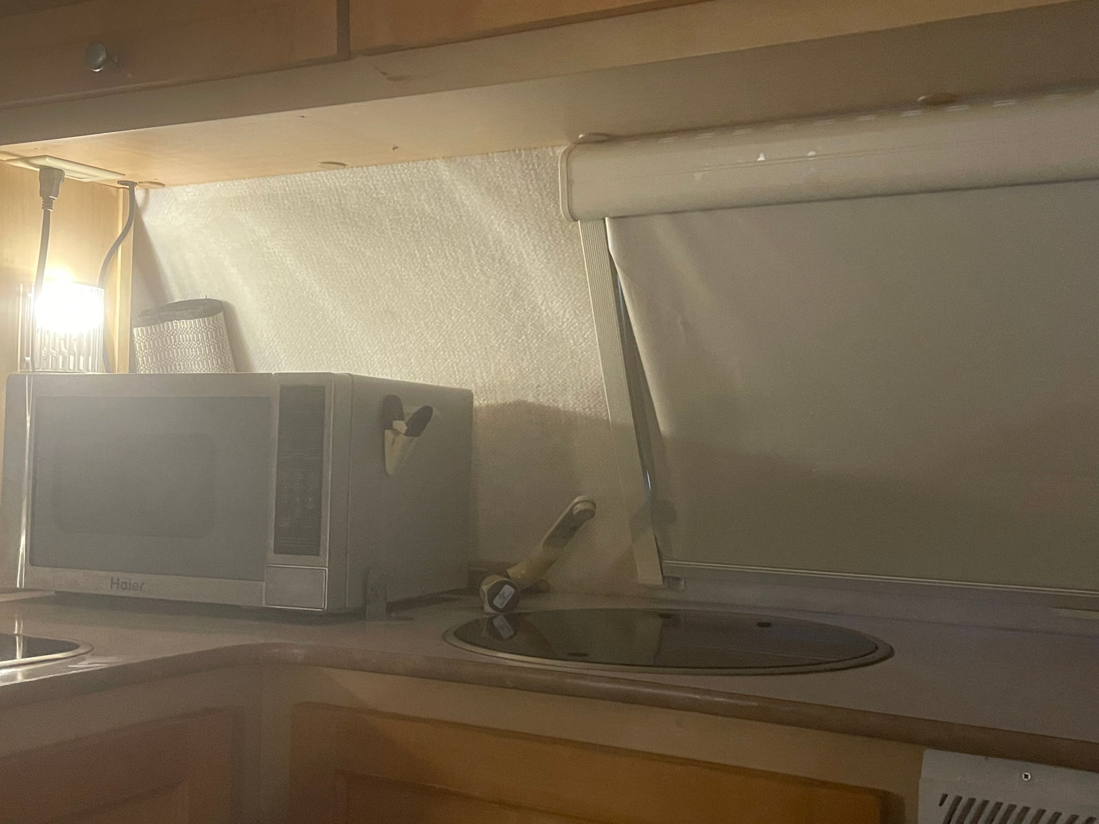 Compact RV rental kitchen with a microwave, covered cooktop, sink, and window blind.