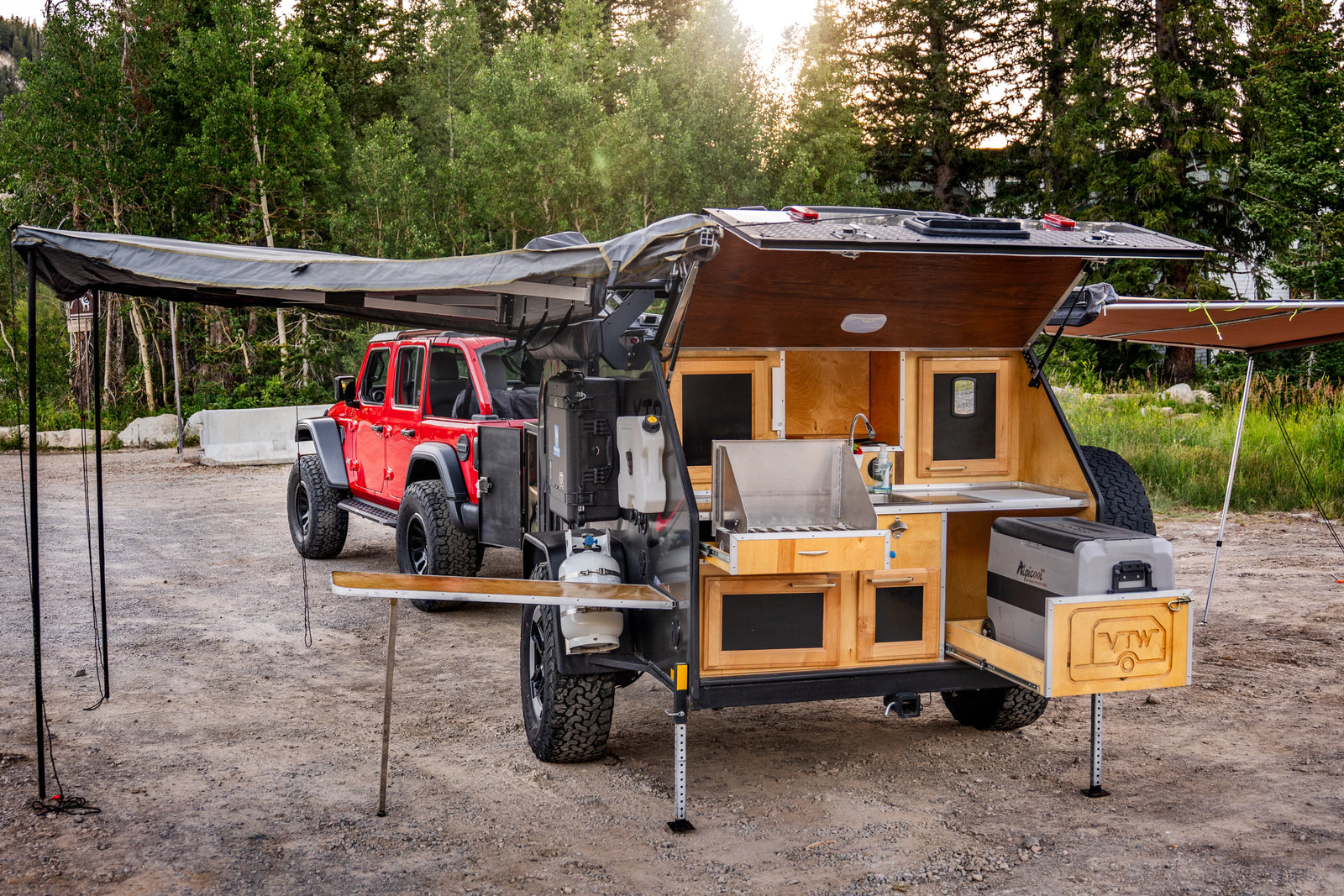 This RV rental setup, featuring a red Jeep and an off-road teardrop camper with a fully equipped outdoor kitchen, is ready for overlanding.