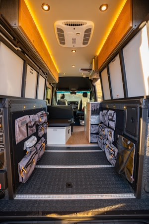 This rv rental van interior features organized side storage, a textured floor, overhead lighting, and an AC unit.