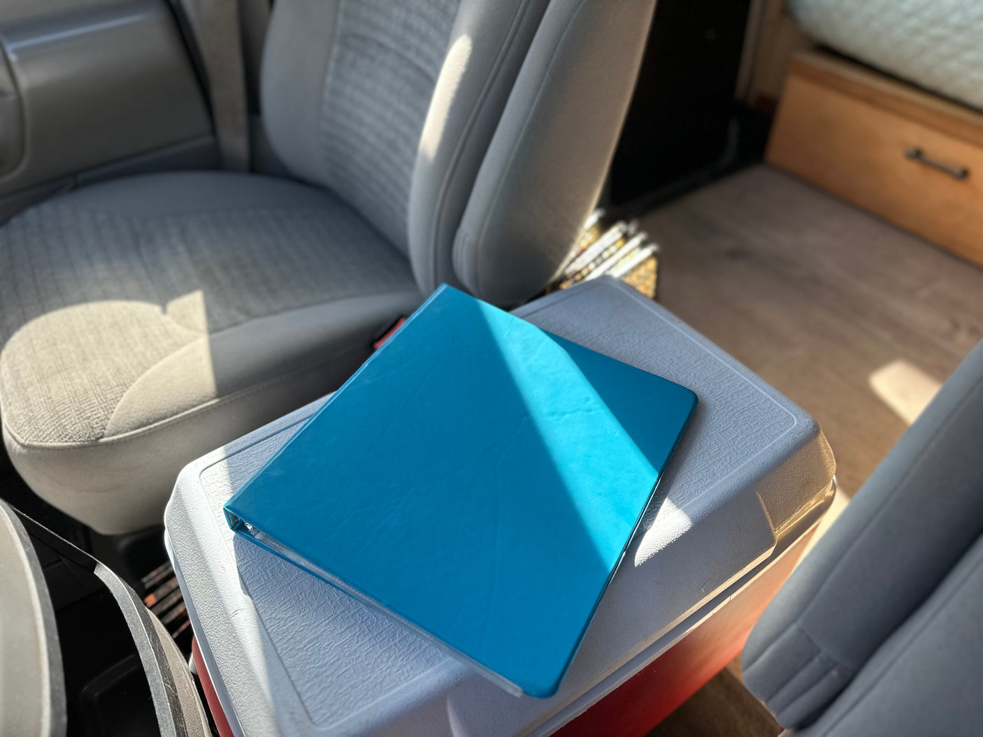 Bright blue binder on cooler in an RV rental, showing front seats and living area detail.