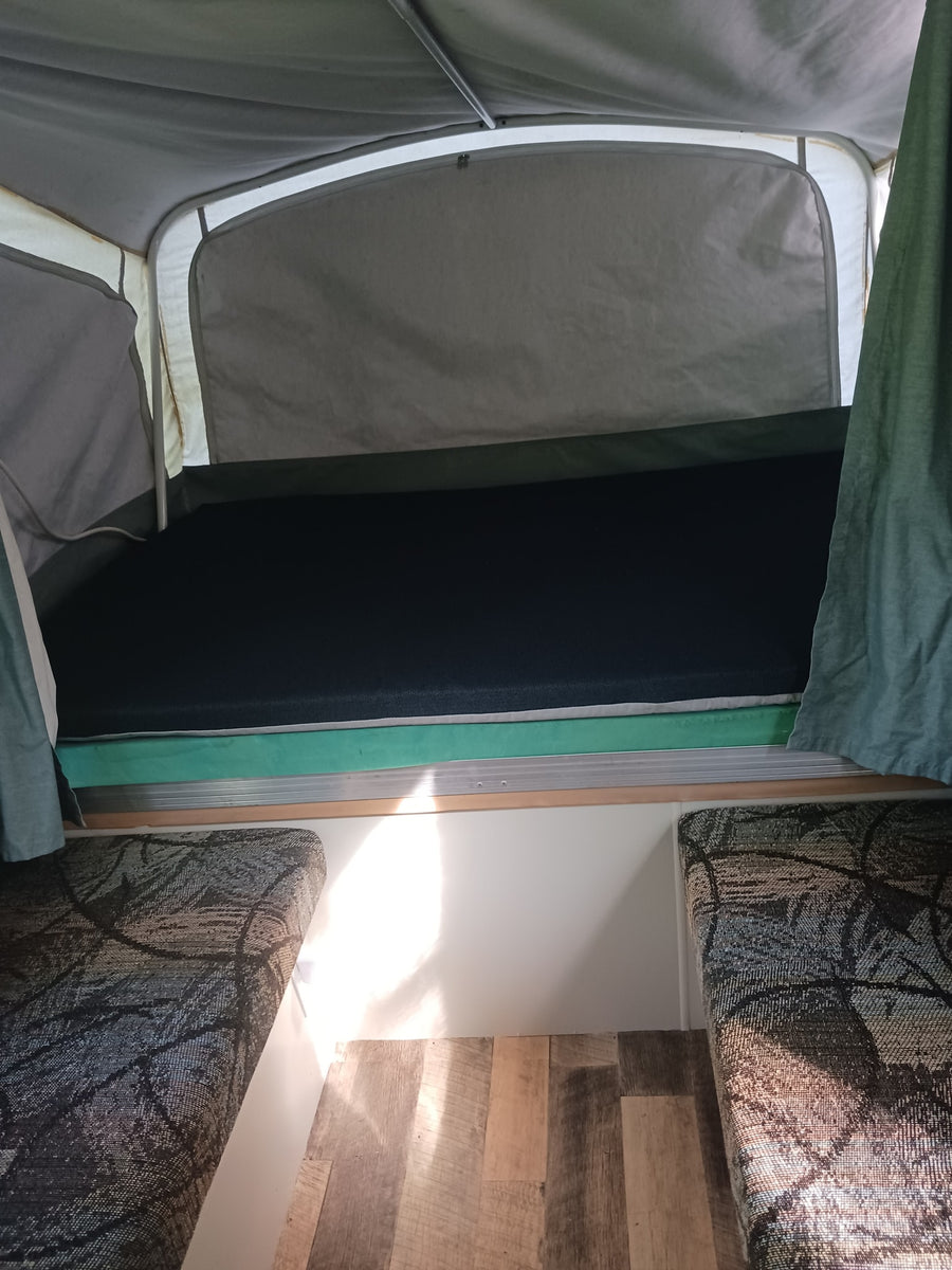 Pop-up RV rental interior: featuring a comfortable bed, patterned seating, and wood-look flooring.