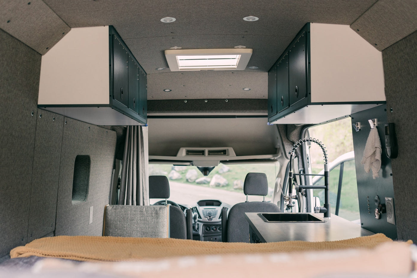 Modern rv rental van interior with kitchen sink, overhead cabinets, and front seats, offering a compact living space. — photo 14