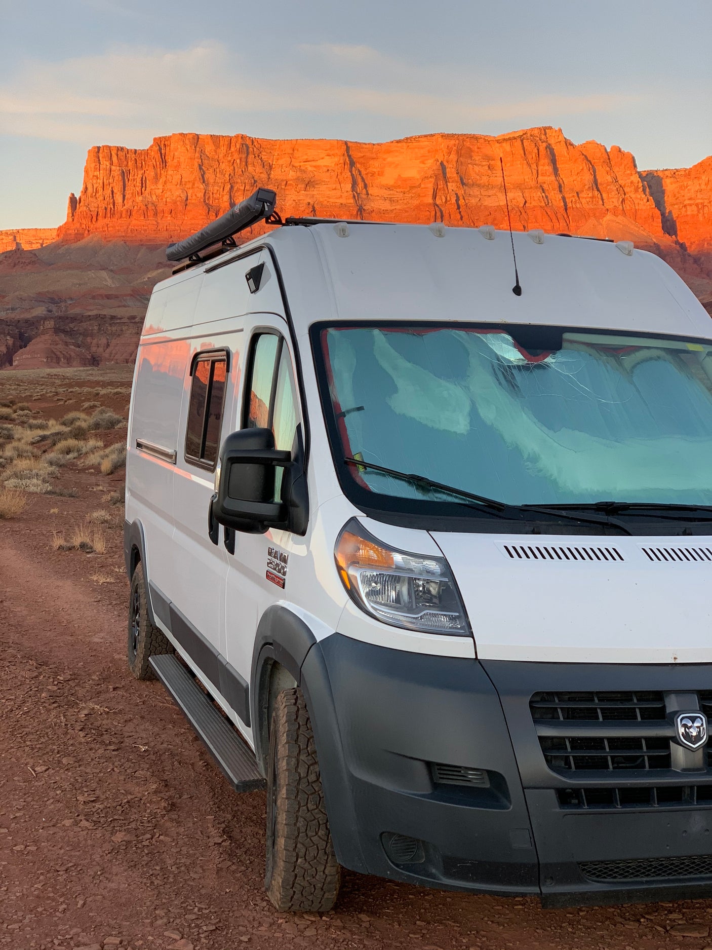 White Ram ProMaster RV rental parked in front of stunning red rock cliffs at sunset. Perfect for adventure!