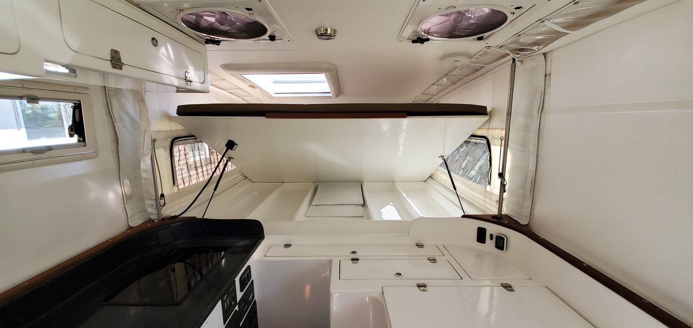 Clean RV rental interior showing a raised bed, compact galley, and white storage compartments.