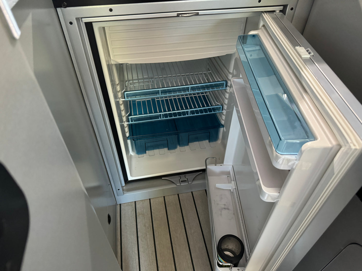 Clean, open RV rental refrigerator, showcasing interior shelves, blue drawers, and door compartments for your travel needs.