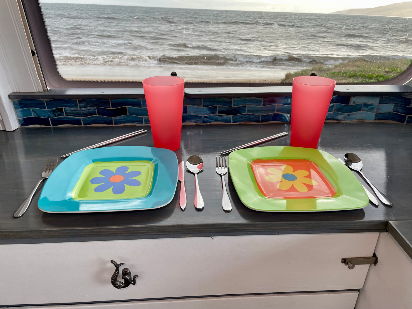 RV rental dining area with vibrant floral plates, cups, and cutlery, offering a stunning ocean view.
