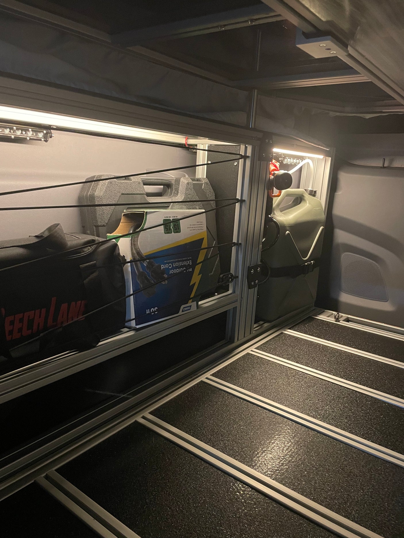 Organized RV rental interior: modular storage with camping gear, extension cord, jerry can, and LED lighting.