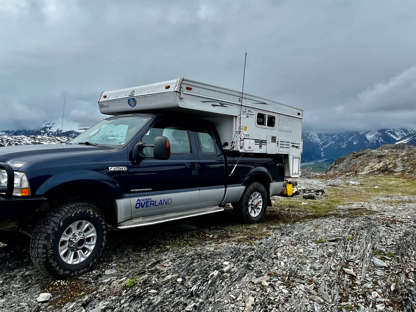 mud-splattered pickup truck with a mounted Bronco truck camper. Ideal for an adventurous RV rental exploring remote landscapes.|A rugged truck camper at the NWT border sign
