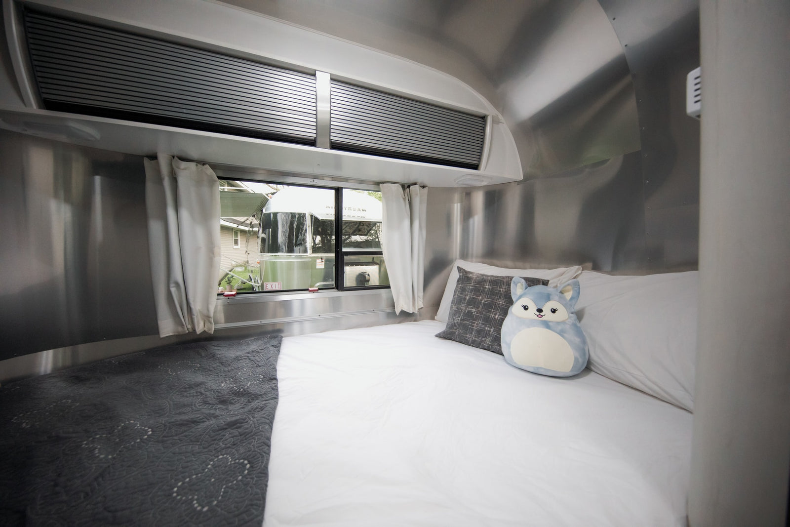 Cozy Airstream rv rental bedroom interior with bed, windows, and plush toy. Perfect for travel!