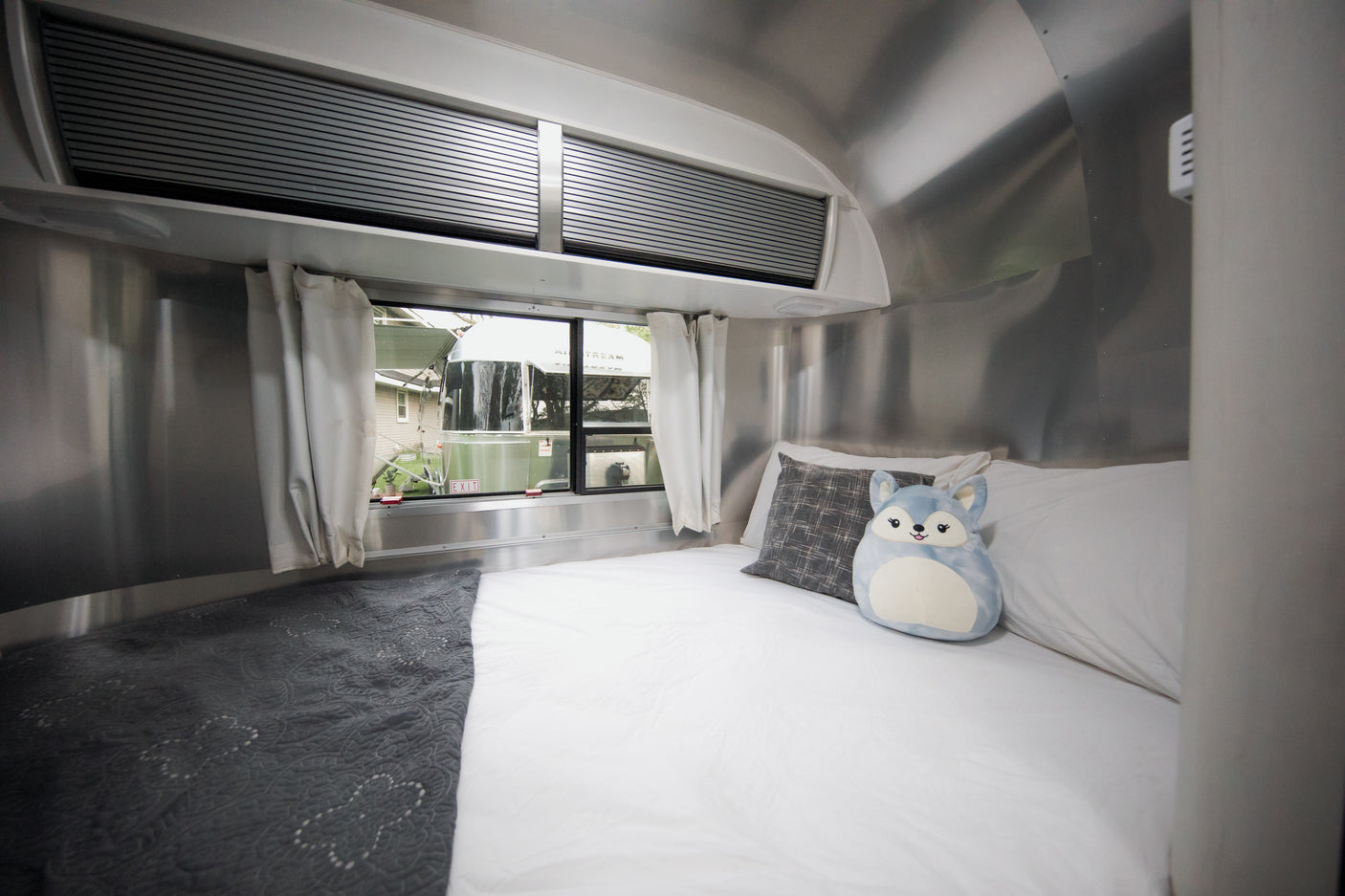 Cozy Airstream rv rental bedroom interior with bed, windows, and plush toy. Perfect for travel!