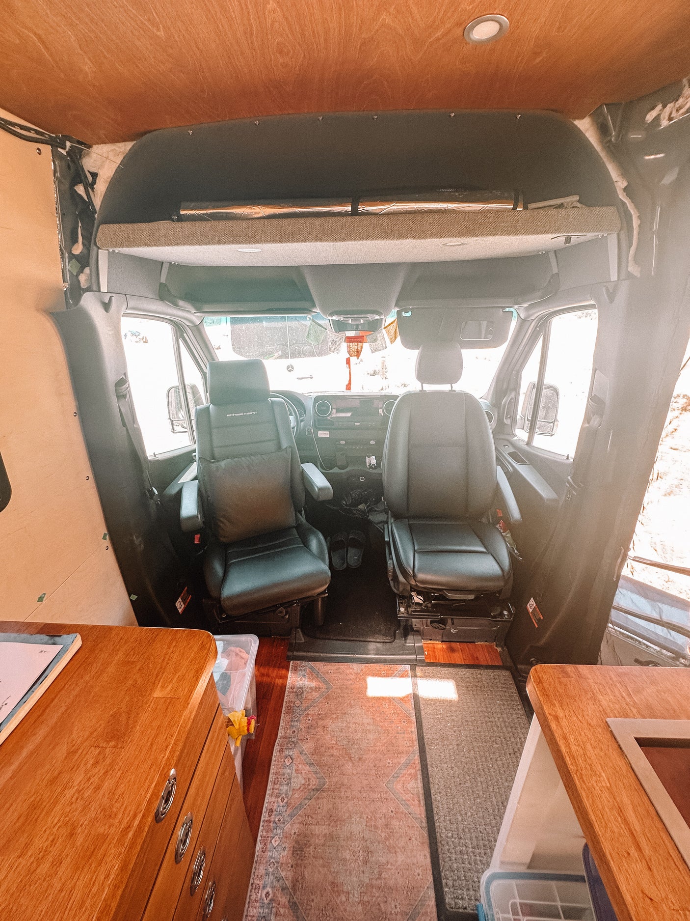 Spacious RV rental interior: custom camper van front cabin with black seats, wood ceiling, and cozy conversion.
