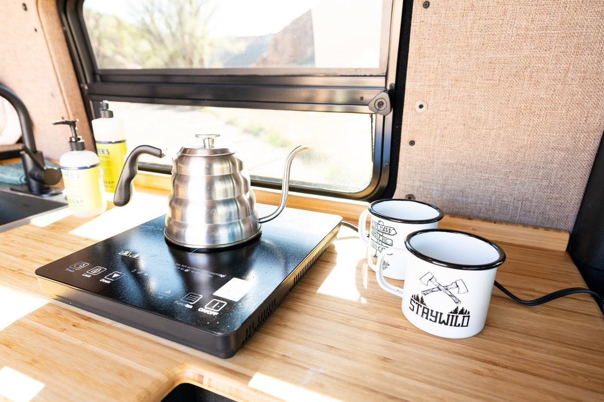 RV rental kitchen: Kettle on induction cooktop, Mrs. Meyer's soaps, & 'Staywild' mugs on wood counter. Ready for adventure. — photo 12
