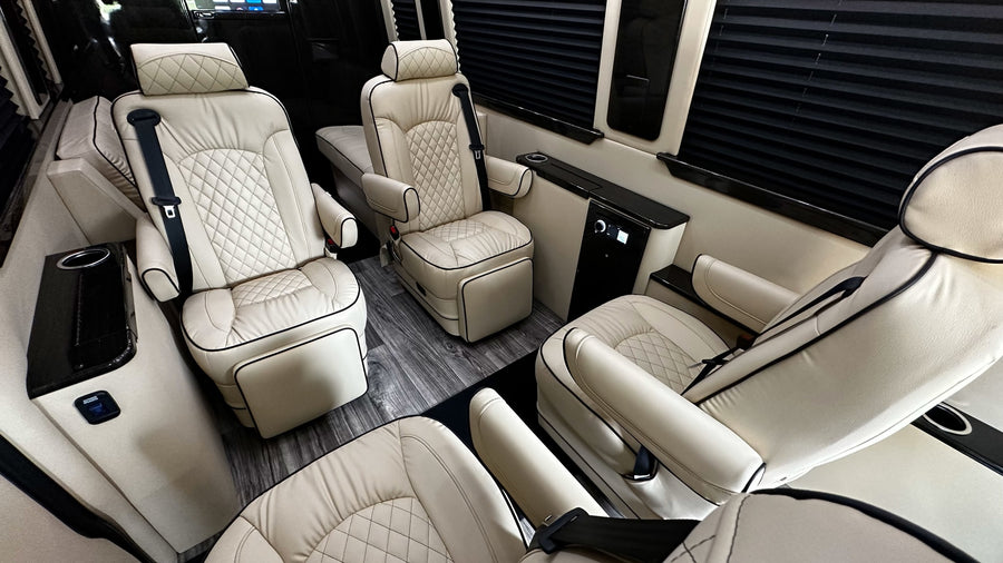 Spacious RV rental interior with cream quilted leather reclining seats, wood-look floor, and privacy blinds for luxurious travel.