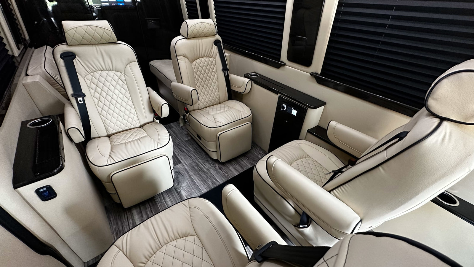 Spacious RV rental interior with cream quilted leather reclining seats, wood-look floor, and privacy blinds for luxurious travel.