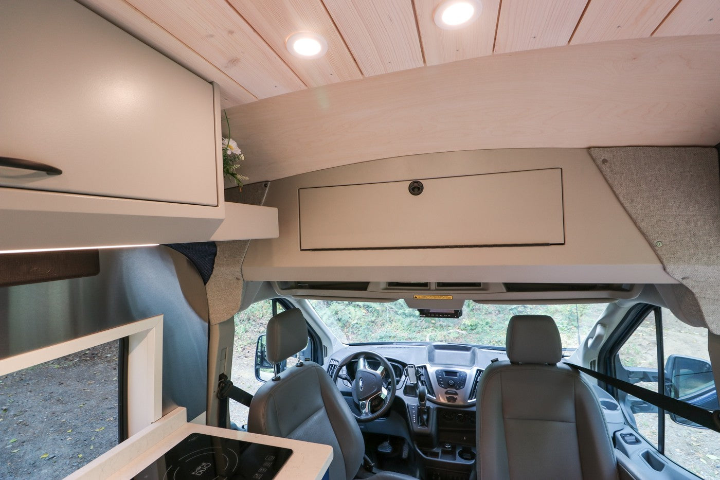 RV rental interior shows a spacious camper van cab, kitchen counter with cooktop, wood ceiling, and overhead storage.