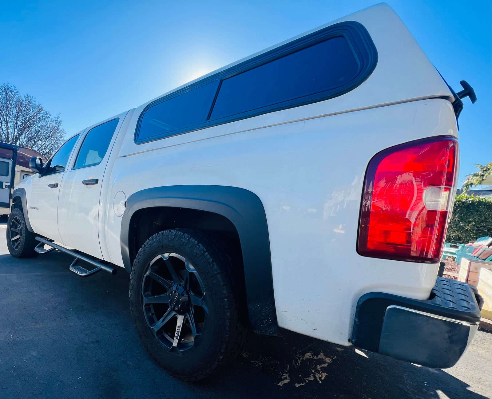 White pickup truck with camper shell, parked by an RV. Offers versatility for your next travel adventure or RV rental trip.