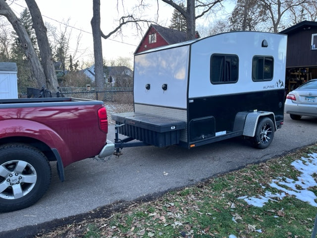 Red pickup truck tows compact, black & white RV rental camper trailer on driveway.
