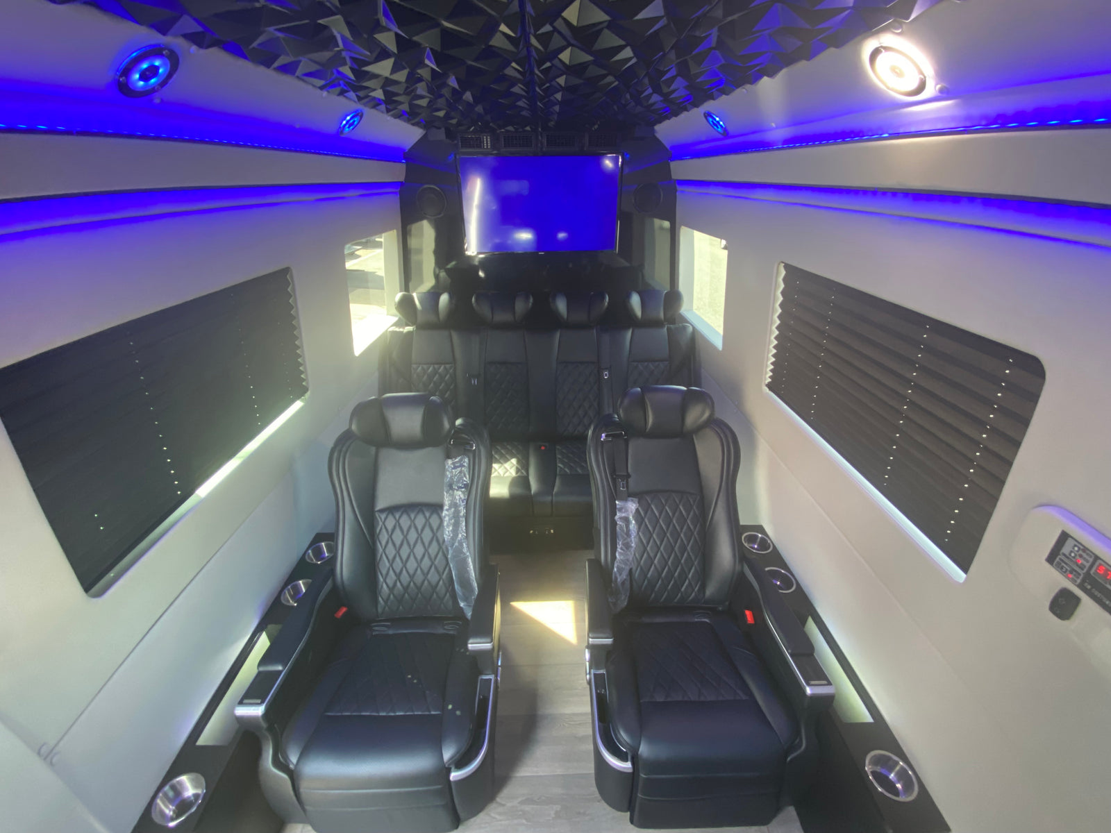 Luxury RV rental interior with black leather captain's chairs, blue LED lighting, a faceted ceiling, and entertainment screen.