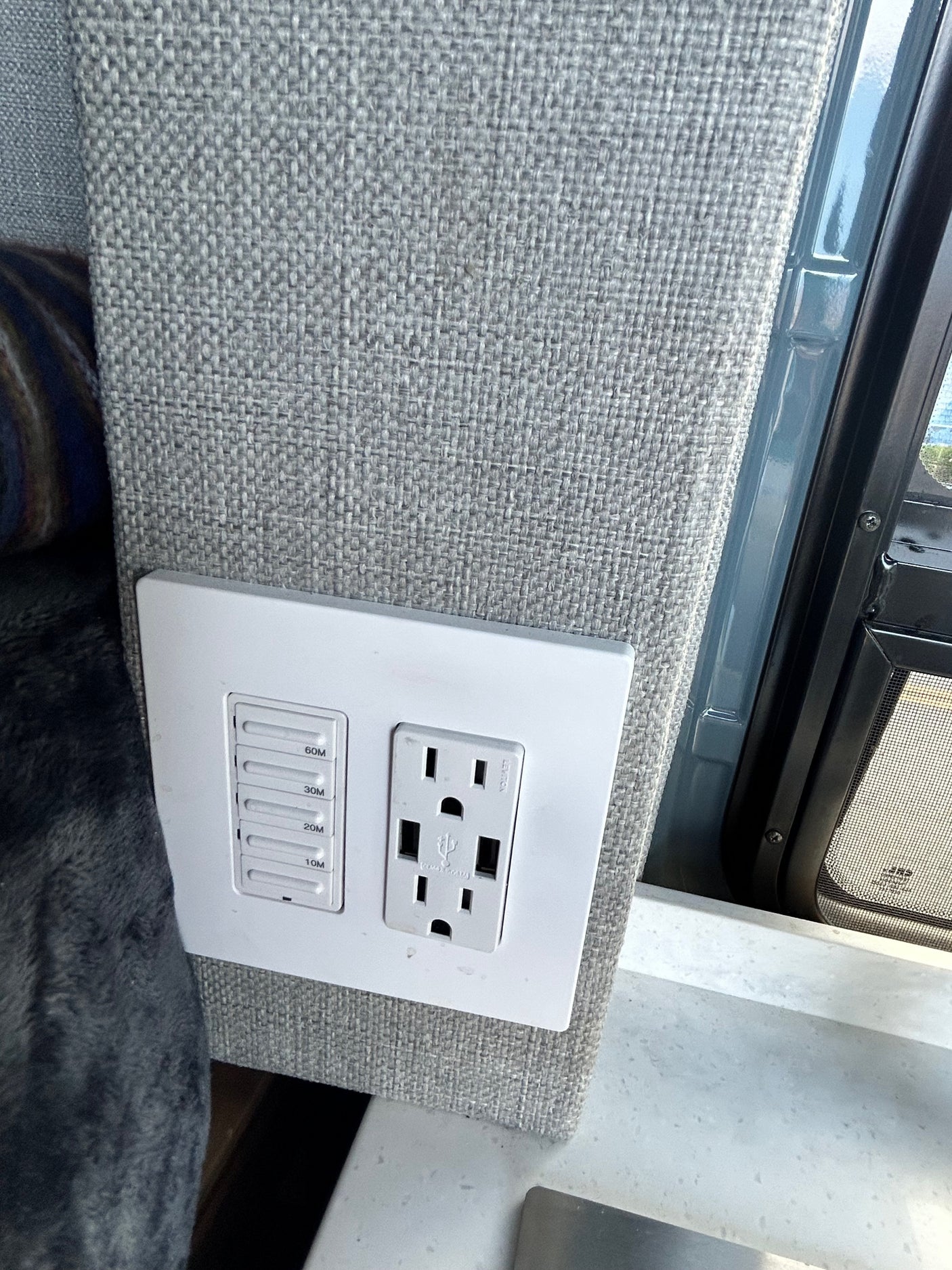 RV rental interior wall: grey fabric with a timer switch (10-60 min) and an electrical outlet featuring USB ports.