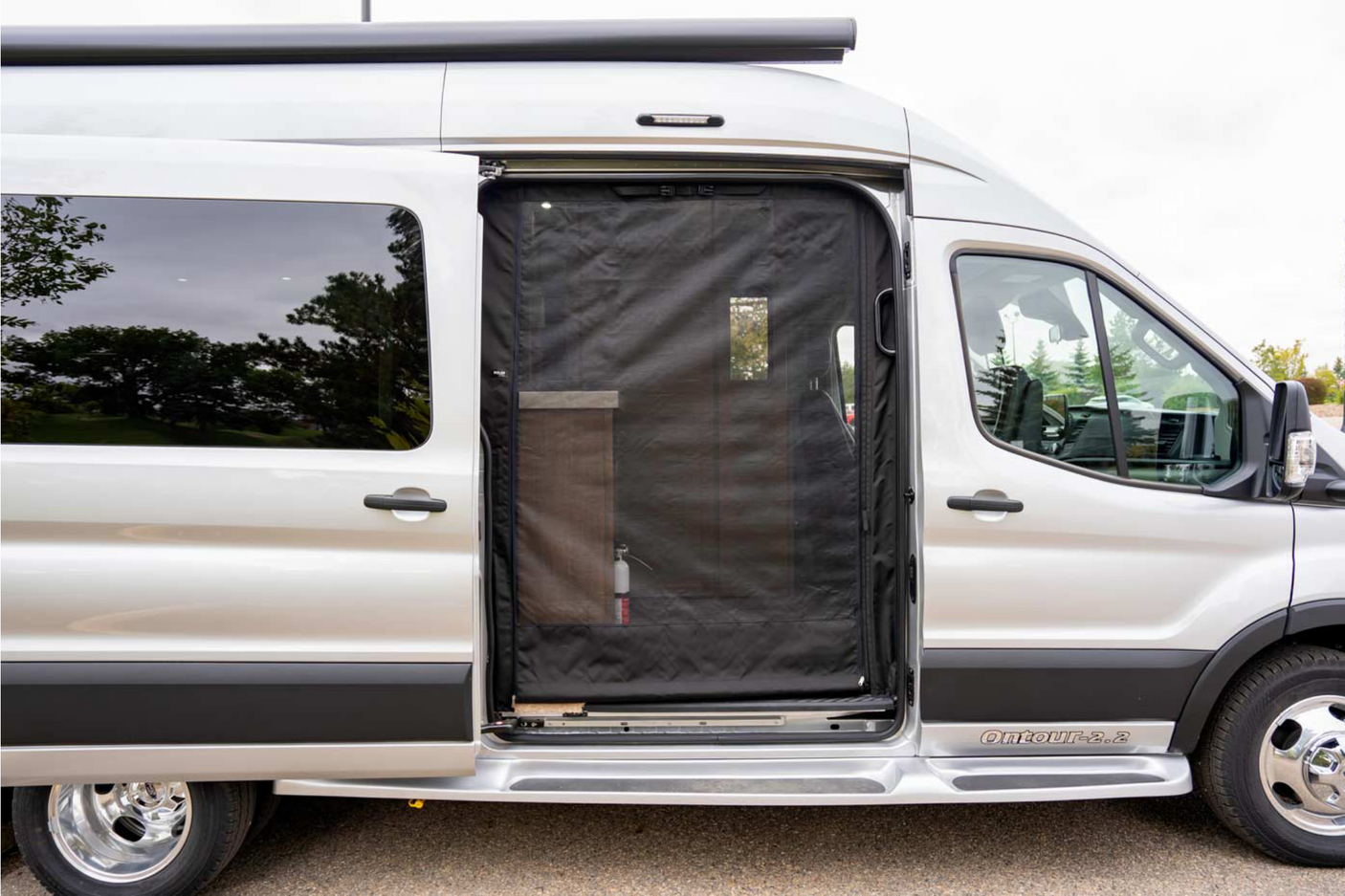 This silver RV rental camper van features an open sliding side door with a black mesh screen, offering a glimpse inside.