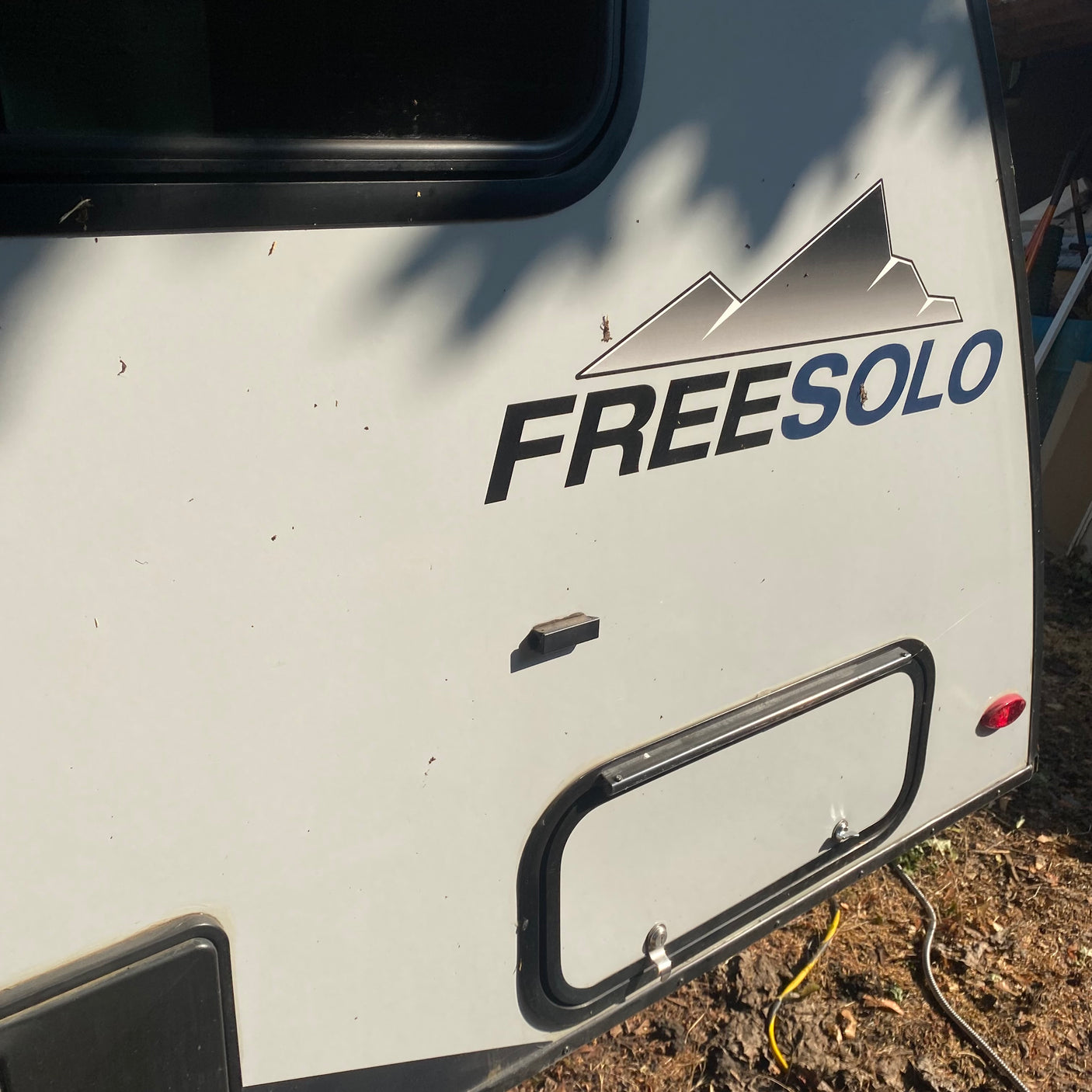 Exterior of a Freesolo RV rental, showing its side, prominent logo, upper window, lower storage hatch, and rear taillight.