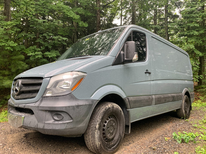 A grey Mercedes Sprinter van, ideal for an RV rental adventure, parked on a damp, muddy forest road.