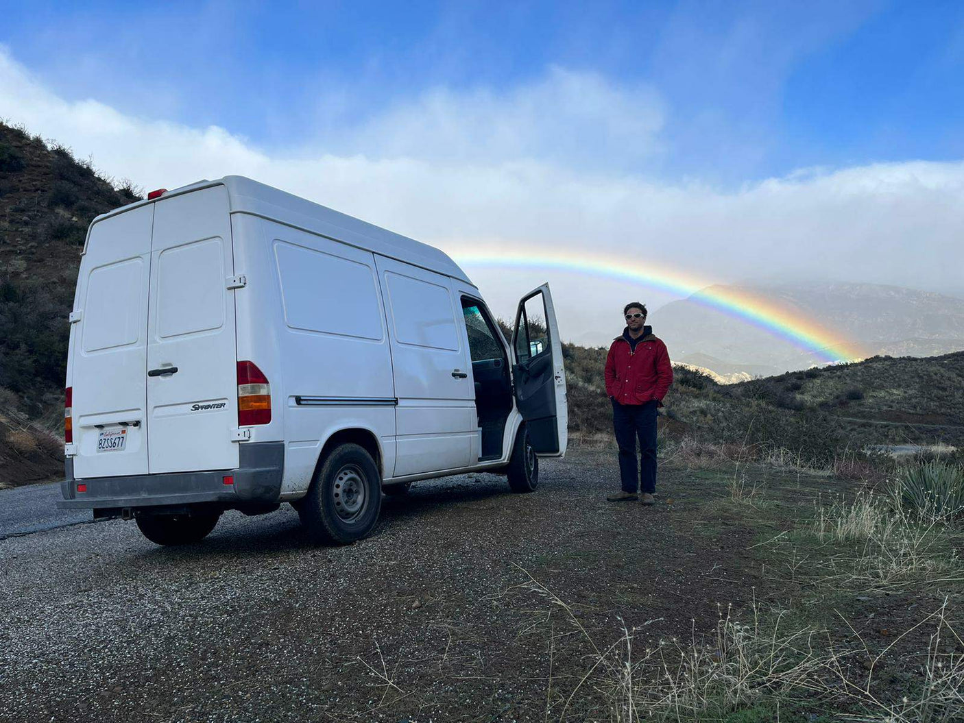 Explore with an RV rental! White Sprinter van, person, & stunning rainbow over mountains. Van life adventures await!