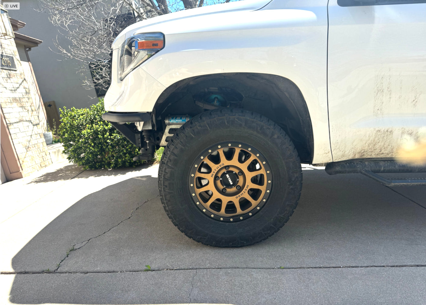 White lifted pickup truck with bronze Method wheels, large off-road tires, and King shocks on a driveway.
